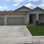 Single-story beige house with three-car garage, concrete driveway, and manicured lawn under blue sky