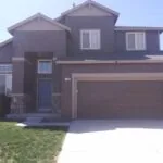 Two-story dark gray house with two-car garage, blue front door, and manicured lawn under clear sky