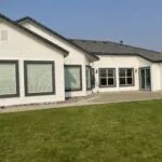 Modern white house with dark roof and black-framed windows overlooking manicured lawn